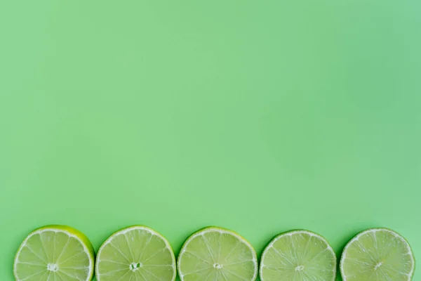 Top view of slices of limes on green background with copy space — Fotografia de Stock