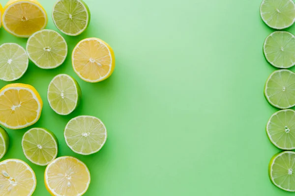 Top view of cut and slices of lemons and limes on green background — стоковое фото