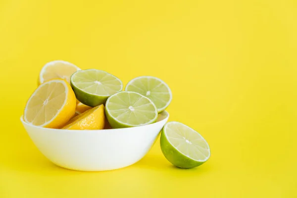 Fresh halves of limes and lemons in bowl on yellow background — Stock Photo