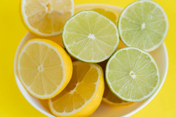 Vue du dessus des citrons frais et des citrons verts dans un bol sur fond jaune — Photo de stock