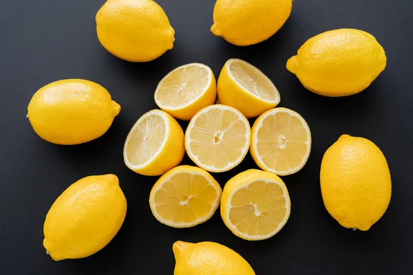 Flat lay with cut and whole lemons on black background — Stock Photo
