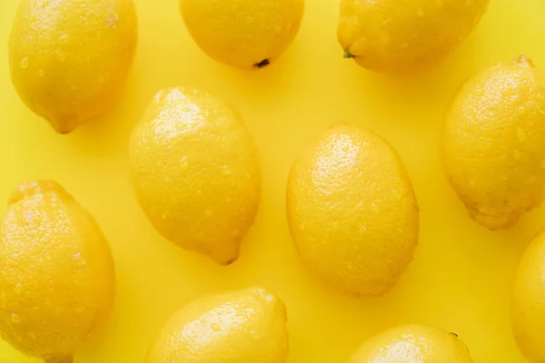 Vista superior de limões frescos com gotículas na casca na superfície amarela — Fotografia de Stock