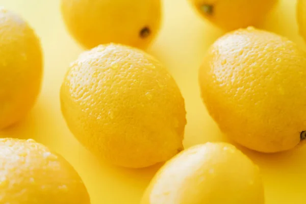 Close up view of organic and wet lemons on yellow surface - foto de stock