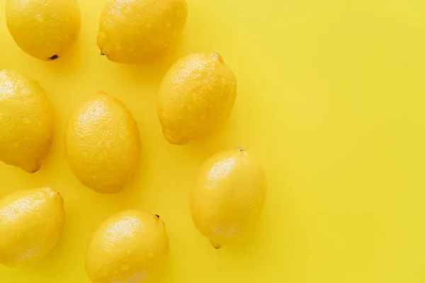 Vista superior de limões maduros com gotas de água na casca na superfície amarela — Fotografia de Stock