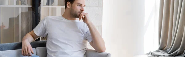 Young man with hand near face looking away while thinking at home, banner — Stock Photo