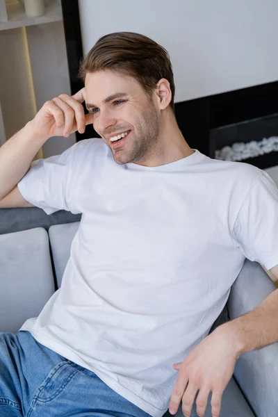 Веселый мужчина в белой футболке сидит и смотрит на дом — стоковое фото