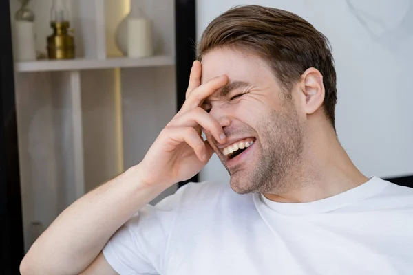 Animado homem em branco t-shirt obscurecendo rosto com a mão enquanto ri de casa — Fotografia de Stock