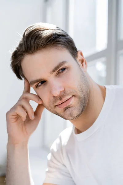 Verträumter und positiver Mann, der die Hand vor das Gesicht hält, während er wegschaut — Stockfoto