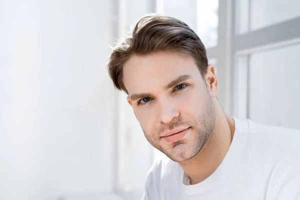 Portrait of young man looking at camera near blurred window — Stock Photo