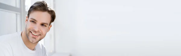 Portrait of young and joyful man looking away near white wall, banner — Stock Photo