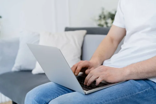 Partial view of man sitting on sofa at home and typing on laptop — Stock Photo