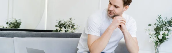 Junger Mann in weißem T-Shirt sitzt im Wohnzimmer mit Blumen dekoriert, Banner — Stockfoto