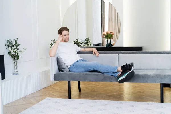 Vue pleine longueur de l'homme rêveur reposant dans le salon décoré de fleurs — Photo de stock