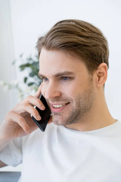 Hombre joven y positivo hablando en el teléfono móvil en casa - foto de stock