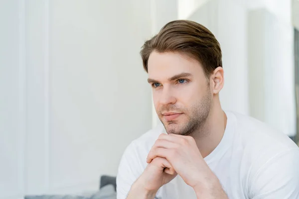 Young man with hands near chin thinking and looking away at home — Stock Photo