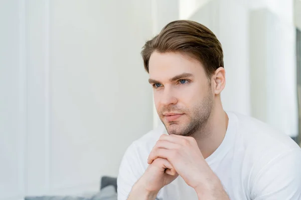 Junger Mann mit Händen in der Nähe des Kinns, der zu Hause wegschaut — Stockfoto