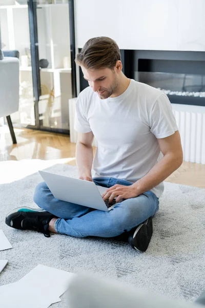 Full length of man sitting on floor with crossed legs and typing on laptop — Stock Photo