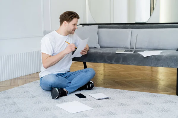 Uomo guardando il computer portatile mentre seduto sul pavimento con carta e matita — Foto stock