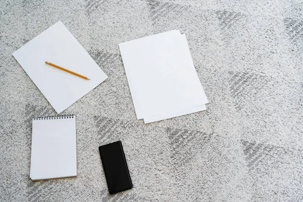 Vue du haut des papiers vides, crayon, cahier et téléphone portable avec écran blanc sur le sol gris — Photo de stock