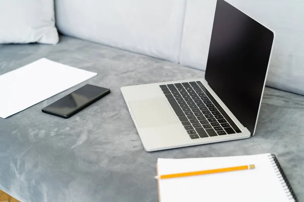 Mobile phone and laptop with blank screen near blurred notebook on grey sofa — Stock Photo