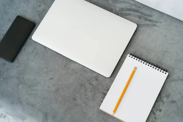 Vista superior de la computadora portátil cerrada, cuaderno vacío con lápiz y teléfono inteligente con pantalla en blanco en la superficie gris - foto de stock