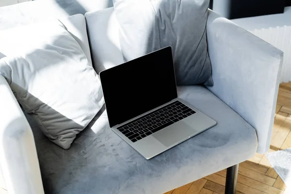 Laptop with blank screen near soft pillows on grey armchair — Stock Photo