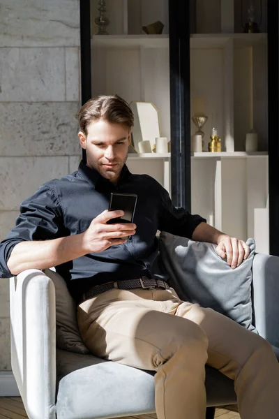 Stilvoller Mann mit Handy sitzt im Sessel im Schatten — Stockfoto