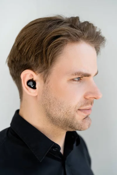 Profil des jungen Mannes, der Musik in drahtlosem Kopfhörer isoliert auf grau hört — Stockfoto