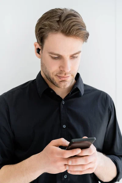 Mann in schwarzem Hemd benutzt Smartphone während er Musik im drahtlosen Kopfhörer hört — Stockfoto
