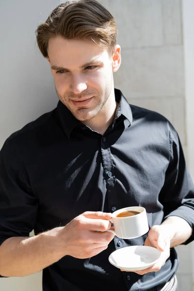 Positive man in black shirt holding morning coffee in shadows — Stock Photo