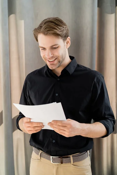 Fröhlicher Mann im schwarzen Hemd, der zu Hause Dokumente liest — Stockfoto