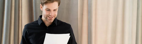 Glücklicher Mann in schwarzem Hemd beim Betrachten von Dokumenten nahe beigem Vorhang, Banner — Stockfoto