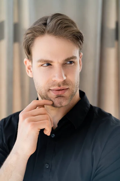 Pensive man in black shirt holding hand near face and looking away at home — Stock Photo