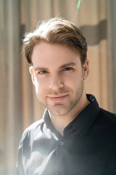 Young man in black shirt smiling at camera in sunshine at home — Stock Photo