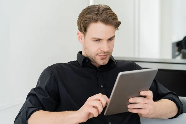Hombre de camisa negra sentado en casa y usando tableta digital - foto de stock