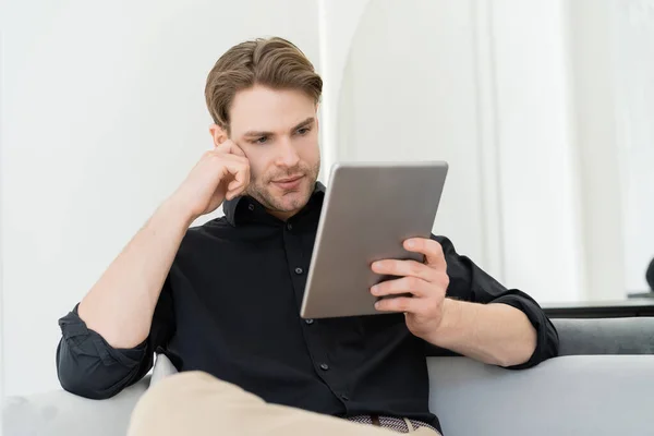 Thoughtful man looking at digital tablet while sitting at home — Stock Photo