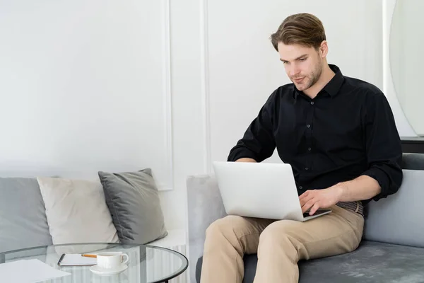 Человек работает на ноутбуке рядом с журнальным столиком с чашкой и ноутбуком — стоковое фото