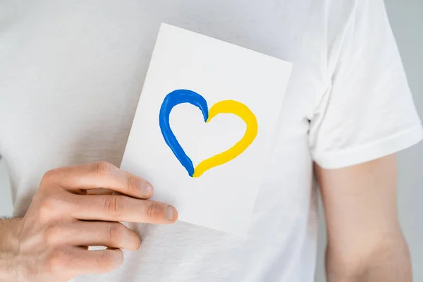 Vista recortada del hombre sosteniendo la tarjeta blanca con la tarjeta azul y amarilla aislada en gris — Stock Photo