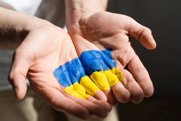 Abgeschnittene Ansicht eines Mannes mit ukrainischer Flagge auf offenen Handflächen isoliert auf schwarz gemalt — Stockfoto