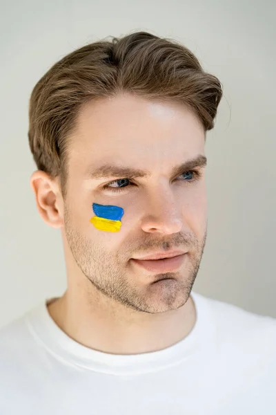 Портрет патріотичного чоловіка з неукраїнським прапором намальованим на обличчі ізольовано на сірому — стокове фото