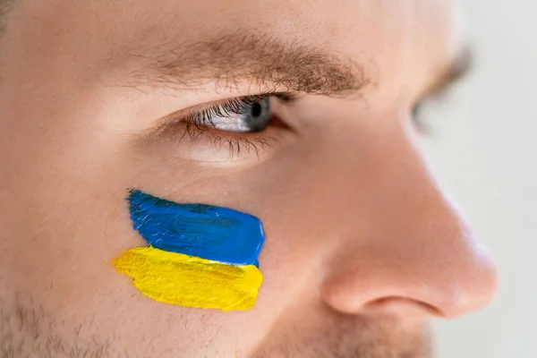 Vista de cerca del hombre con bandera ucraniana pintada en la cara aislada en gris - foto de stock