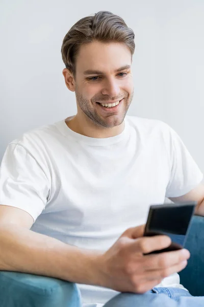 Hombre sonriente en camiseta blanca charlando en el teléfono celular en primer plano borrosa - foto de stock