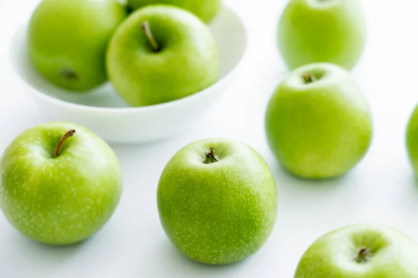 Green and ripe apples near bowl on white — стоковое фото