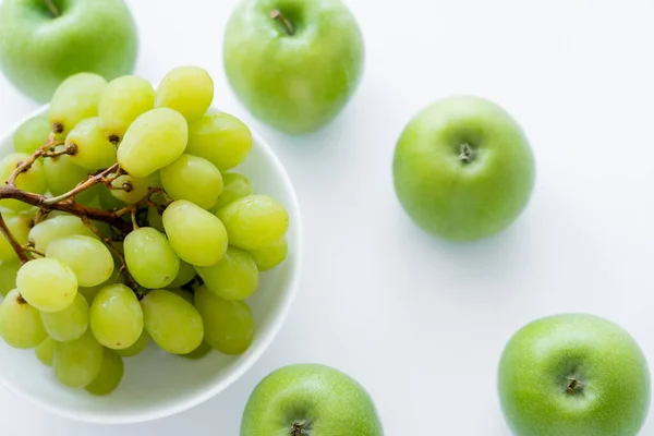 Vista superior de maçãs verdes perto de uvas em tigela em branco — Fotografia de Stock