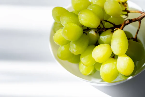Sunshine on green grapes in bowl on white — Stock Photo