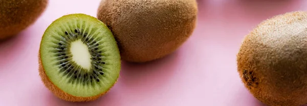 Green kiwi near whole fruit on pink, banner — Stock Photo