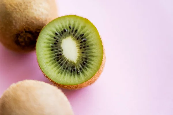 Top view of cut kiwi near whole fruit on pink - foto de stock