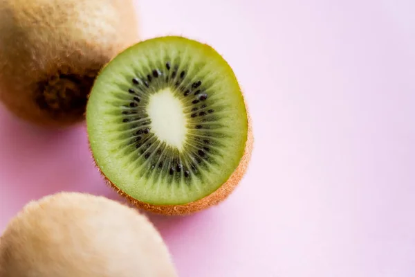 Vista dall'alto di kiwi tagliato vicino a frutto intero su rosa — Foto stock