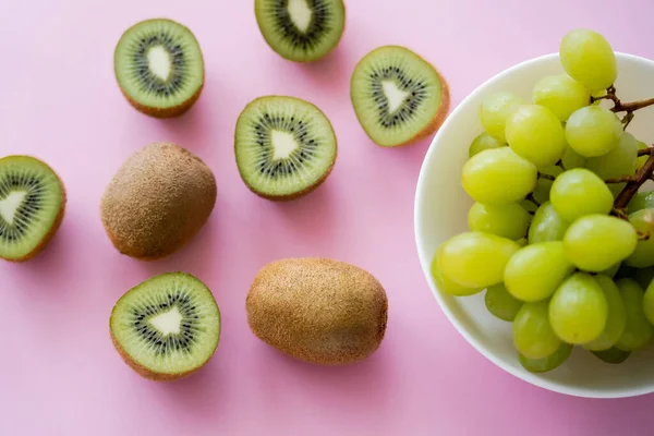 Top view of grapes in bowl near kiwi on pink - foto de stock