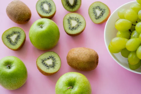 Vue du dessus des raisins dans un bol près du kiwi et des pommes sur rose — Photo de stock